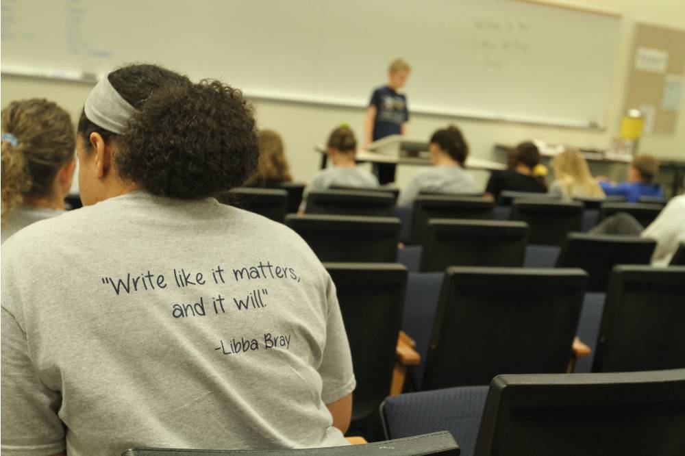 A student wearing a Laker Writing Camp shirt listens to a student present.